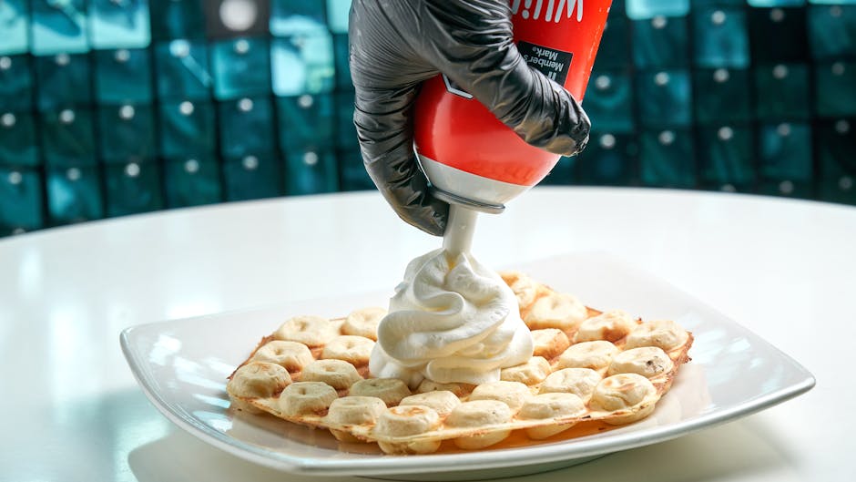 Best waffles in Brussels — close-up of waffle being topped with whipped cream by gloved hand