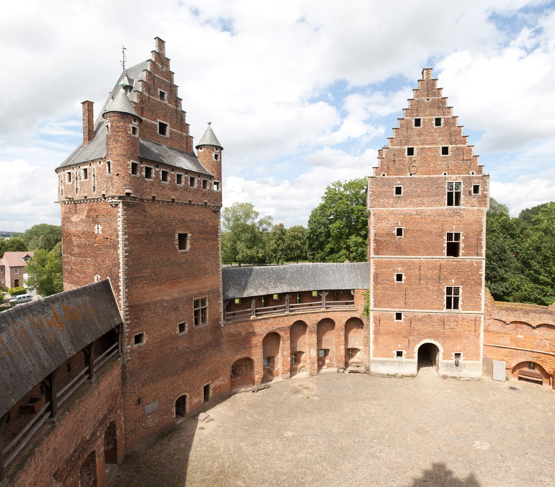The horseshoe-shaped cobbled courtyard of Beersel castle, with two tall red-brick towers topped by stepped gables and a covered wall walk between them