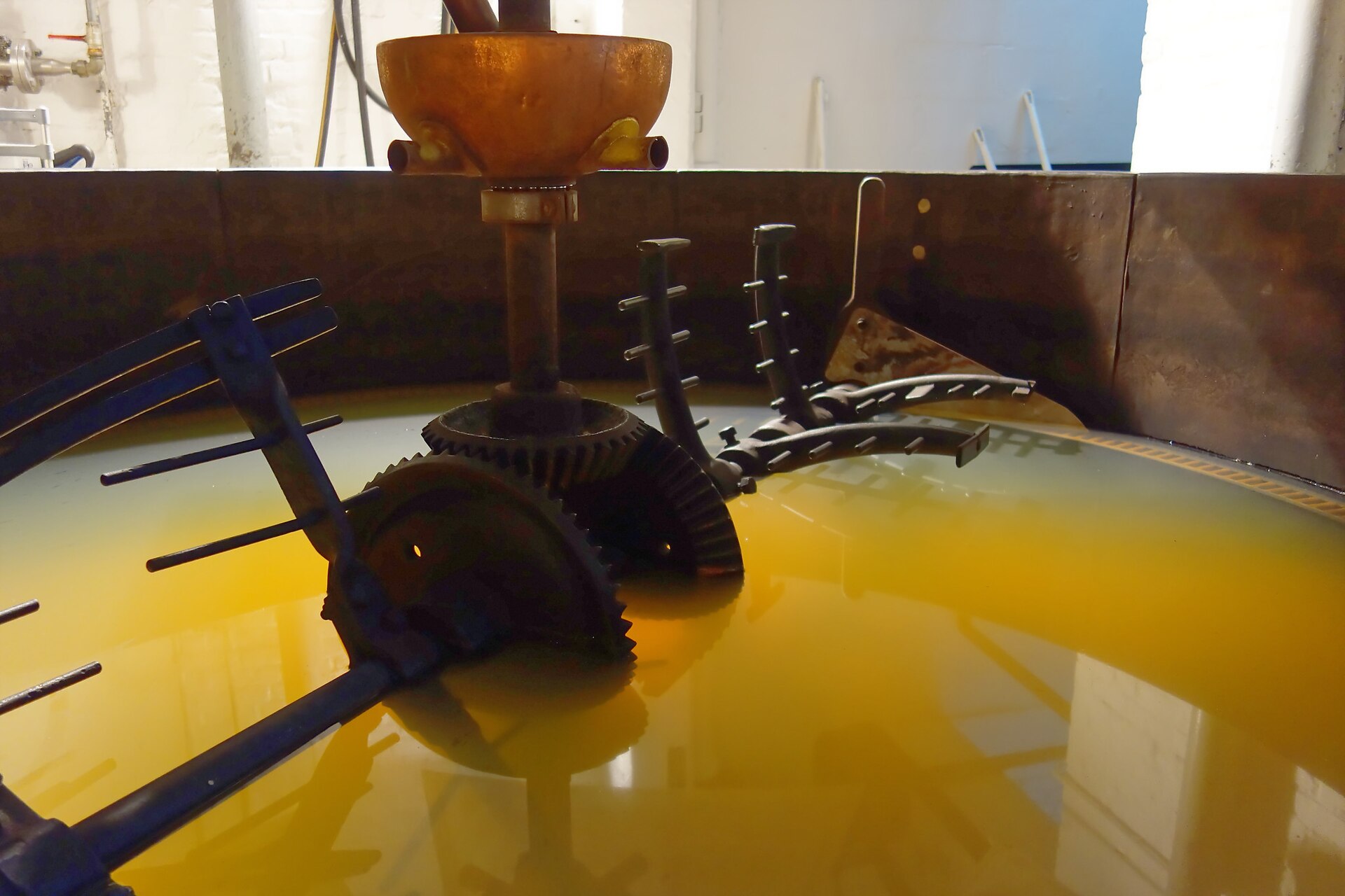 Metal rakes turning through cloudy golden wort in the open mash tun at Cantillon brewery in Brussels