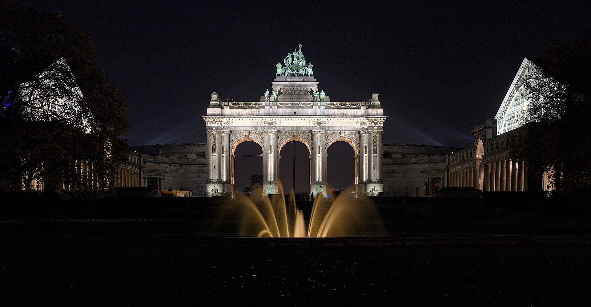 The floodlit triumphal arch at the Parc du Cinquantenaire in Brussels at night with autumn trees