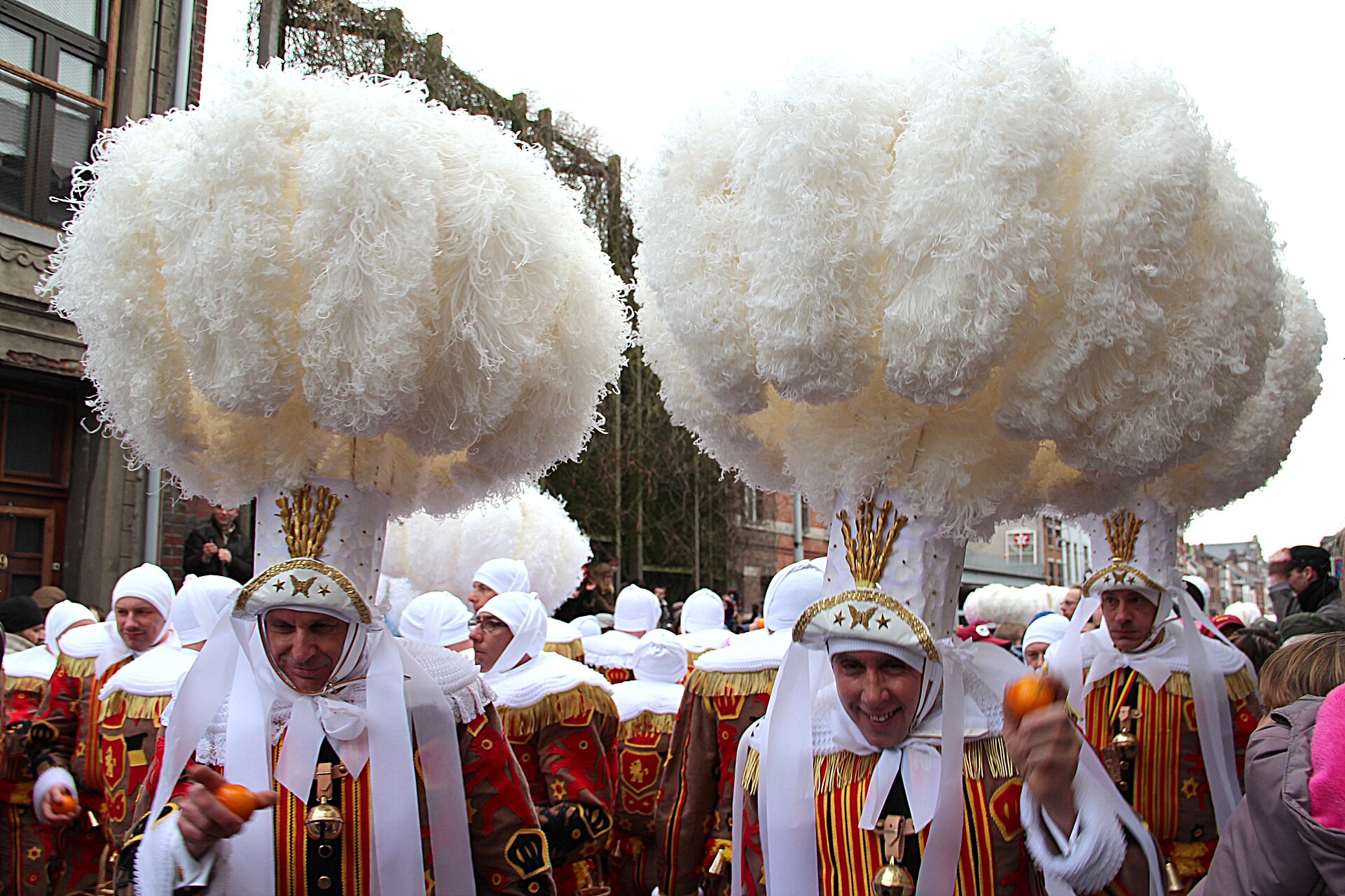 Gilles of Binche in tall white ostrich-feather hats holding oranges during the Shrove Tuesday carnival procession
