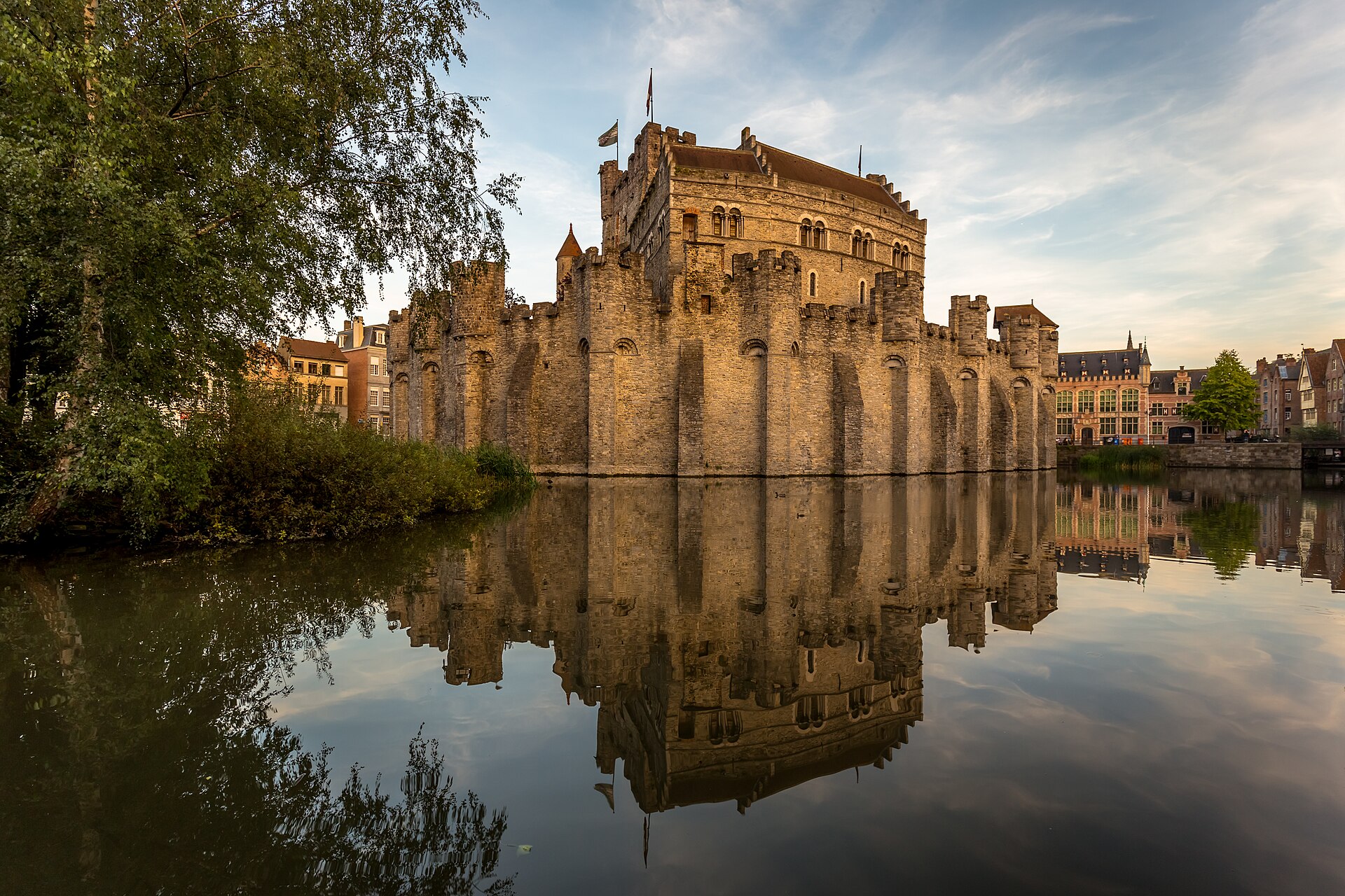 The stone walls and keep of the Gravensteen castle in Ghent reflected in its moat at golden hour