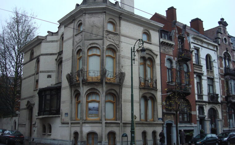 The pale Art Nouveau corner facade of the Hôtel Hannon in Saint-Gilles, with curved bay windows and wrought-iron balconies, on a grey day with bare trees