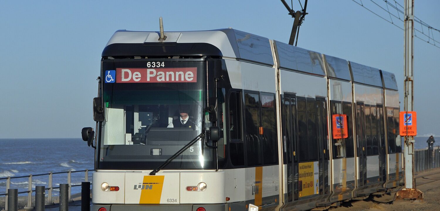 A white and yellow De Lijn coastal tram bound for De Panne running alongside the sea wall on the Belgian coast
