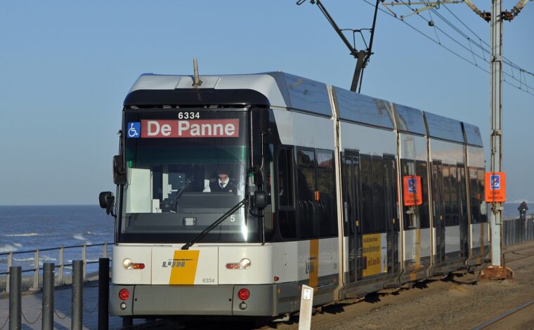 A white and yellow De Lijn coastal tram bound for De Panne running alongside the sea wall on the Belgian coast