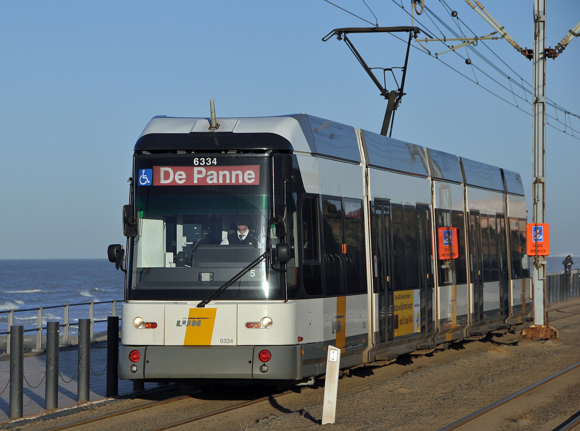 A white and yellow De Lijn coastal tram bound for De Panne running alongside the sea wall on the Belgian coast