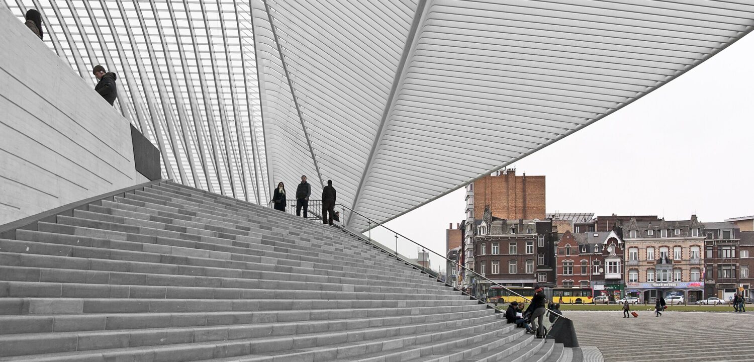 The sweeping white steel ribs of Calatrava's canopy over the broad stone steps of Liège-Guillemins station, with a row of old town houses and a yellow bus beyond