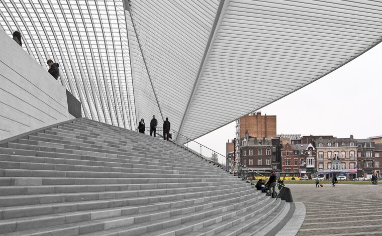 The sweeping white steel ribs of Calatrava's canopy over the broad stone steps of Liège-Guillemins station, with a row of old town houses and a yellow bus beyond