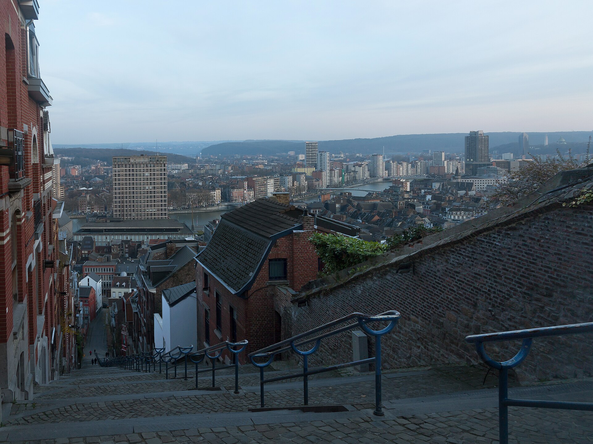 The view down the stone steps and blue railings of the Montagne de Bueren over the rooftops and tower blocks of Liège to the Meuse and the hills beyond