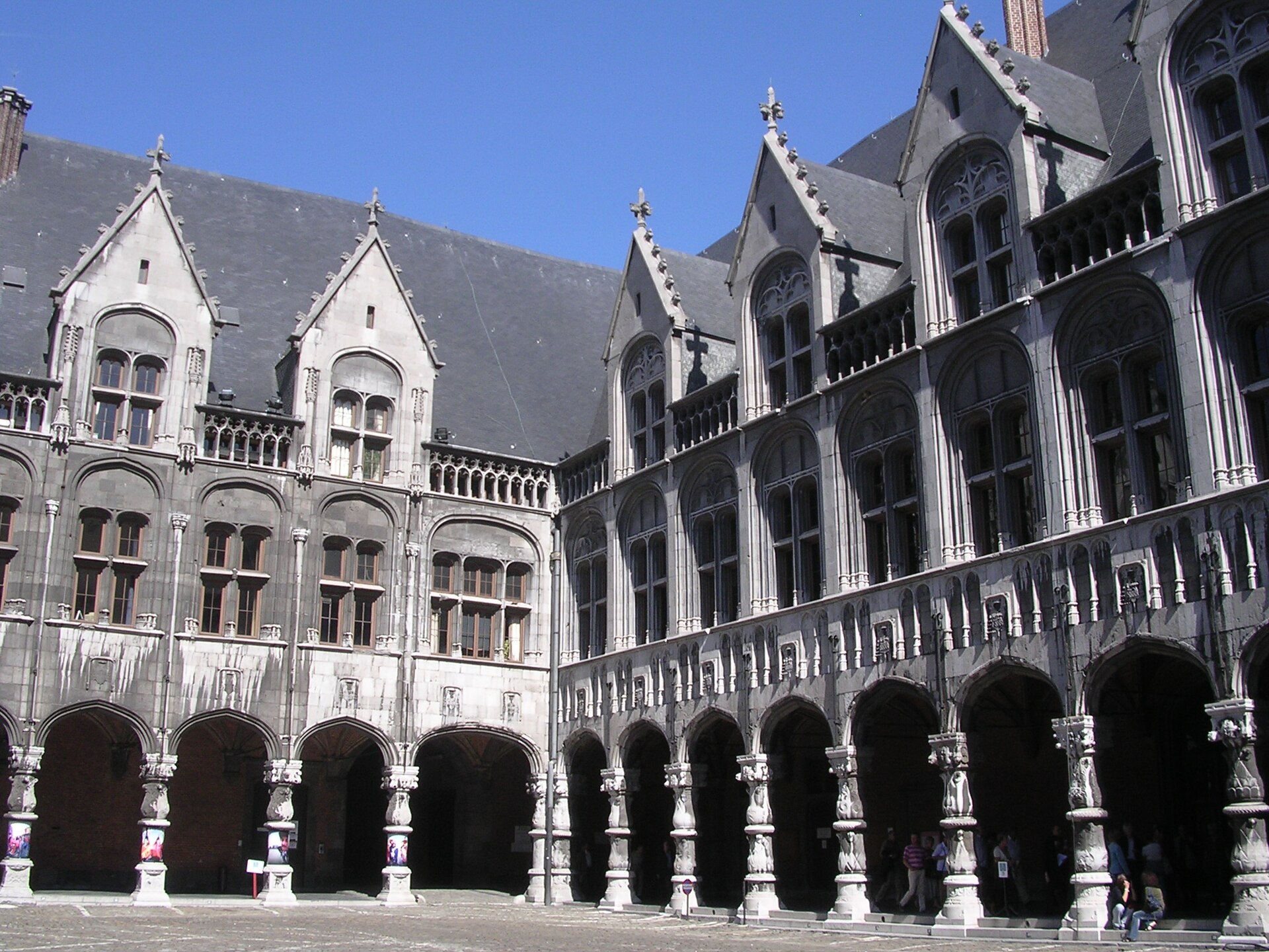 The arcaded courtyard of the Palace of the Prince-Bishops in Liège, with carved stone columns beneath grey stone facades and steep slate roofs