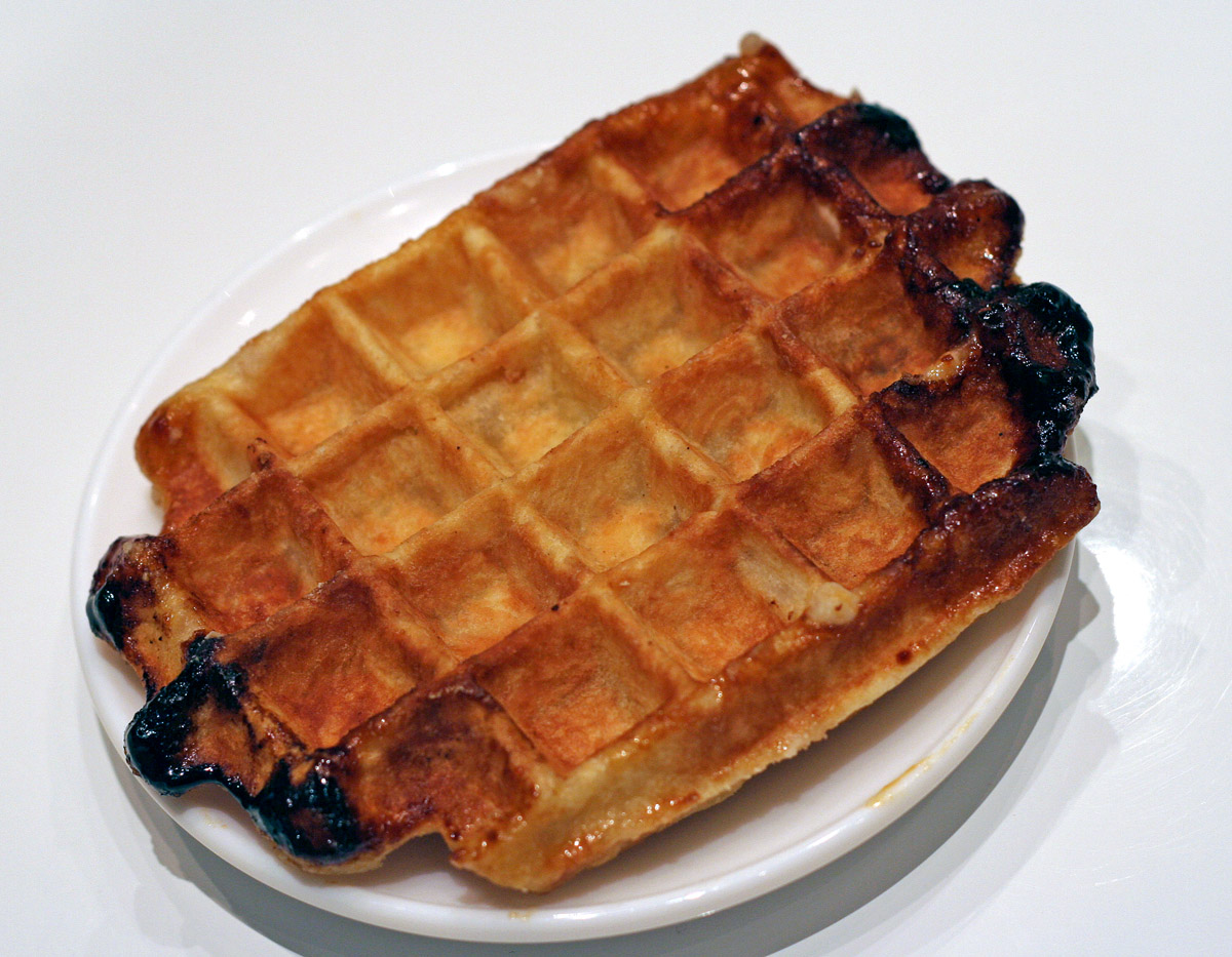 A Liège waffle on a white plate, golden with dark caramelised pearl-sugar edges