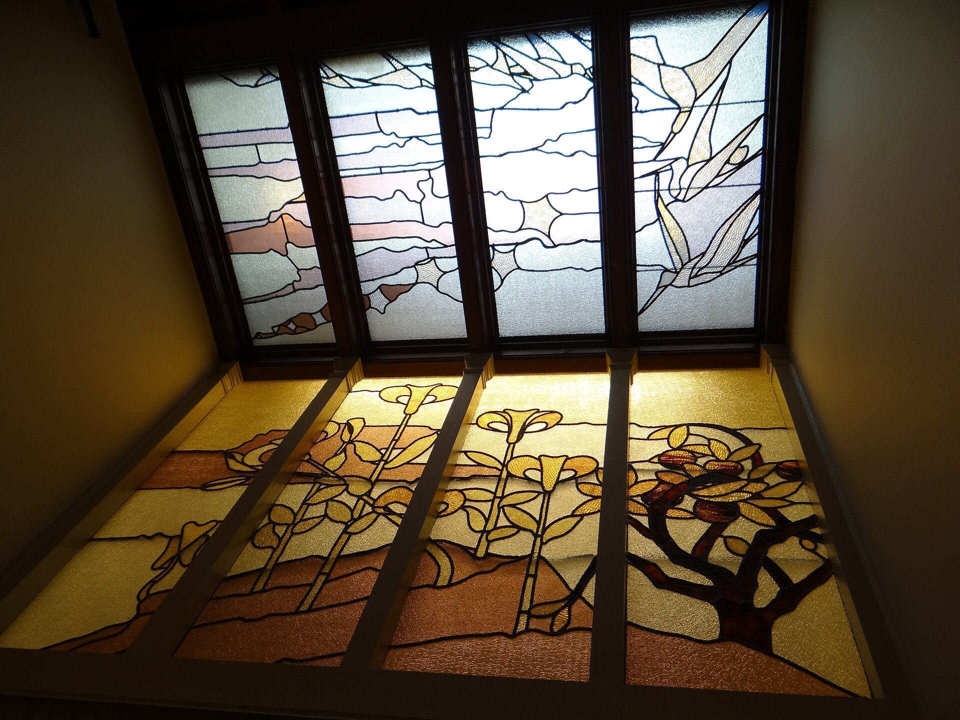 An Art Nouveau stained-glass skylight in the Maison Autrique in Schaerbeek, with stylised yellow flowers and branches beneath a pale glass sky