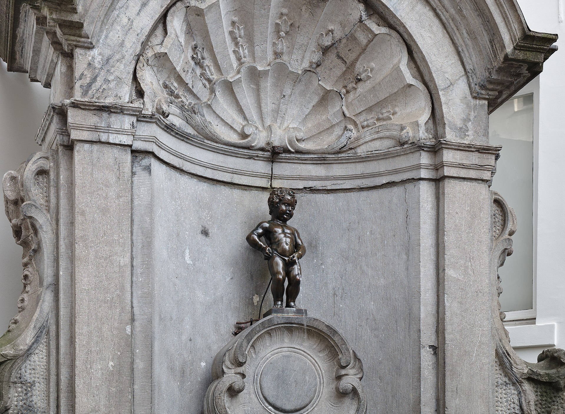The bronze Manneken Pis statue in its stone niche in Brussels, without a costume