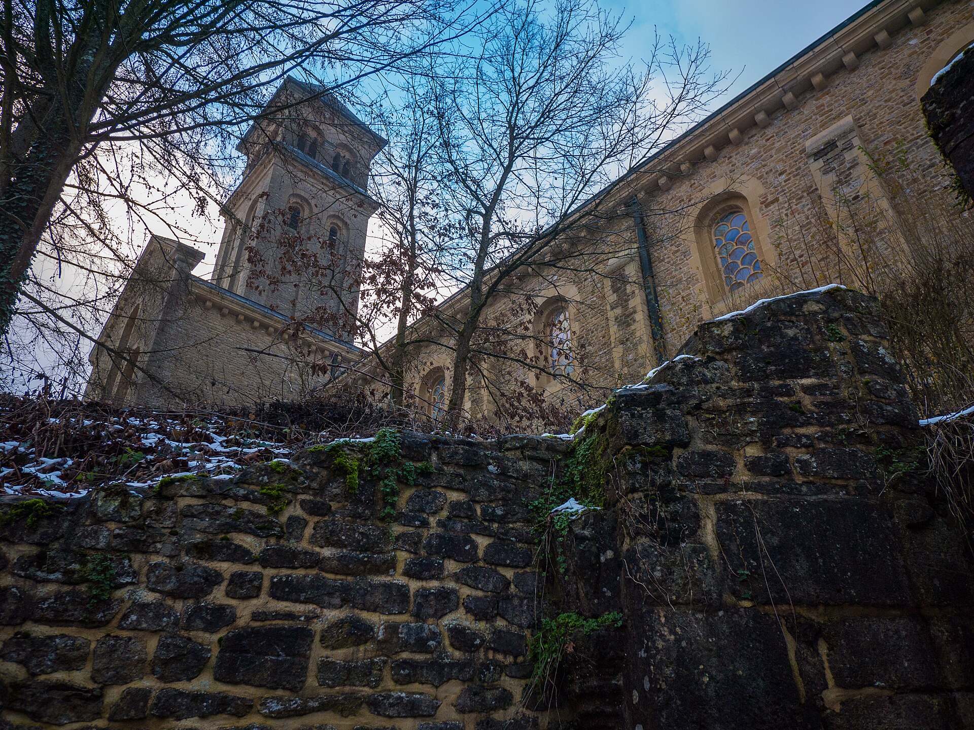 The stone church and tower of Orval Abbey seen over an old moss-covered wall in winter