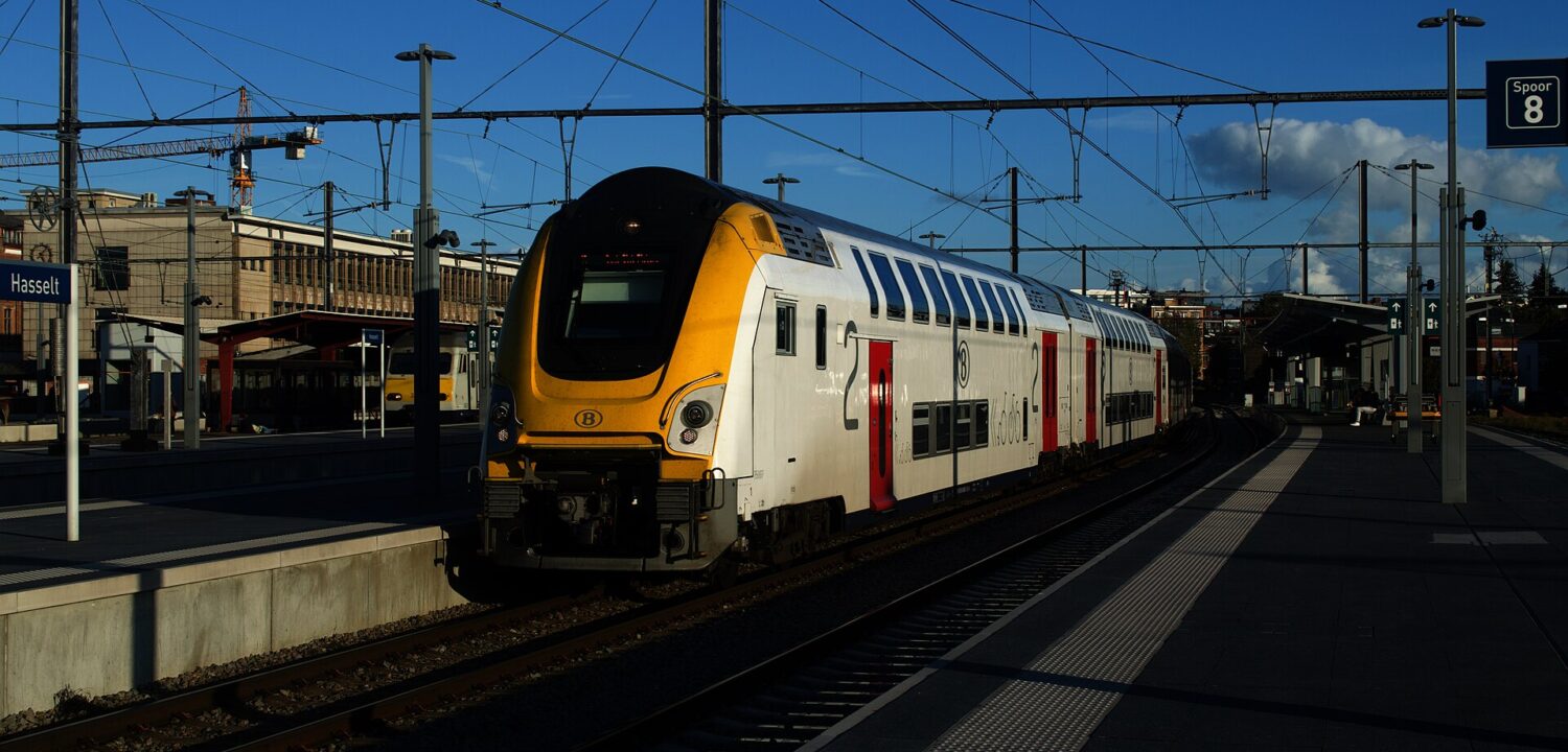 A white and yellow SNCB double-deck intercity train standing at platform 8 of Hasselt station in low evening sun