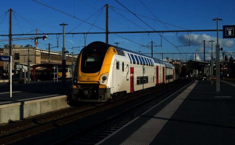 A white and yellow SNCB double-deck intercity train standing at platform 8 of Hasselt station in low evening sun