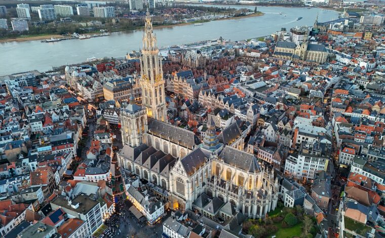 Antwerp Cathedral of Our Lady rises above dense old-town rooftops, with the broad Scheldt river behind its Gothic spire.