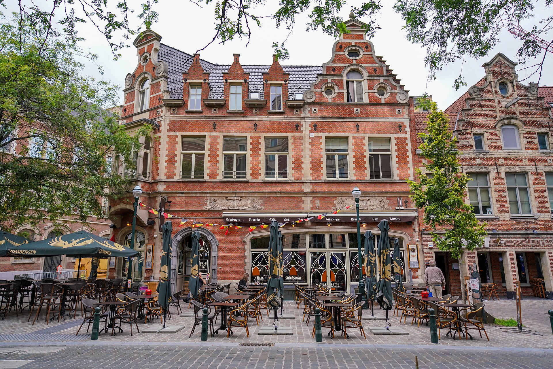 A beer cafe terrace sits beneath ornate red brick gables on Place Sainte-Catherine in Brussels, with Grimbergen umbrellas and outdoor tables.