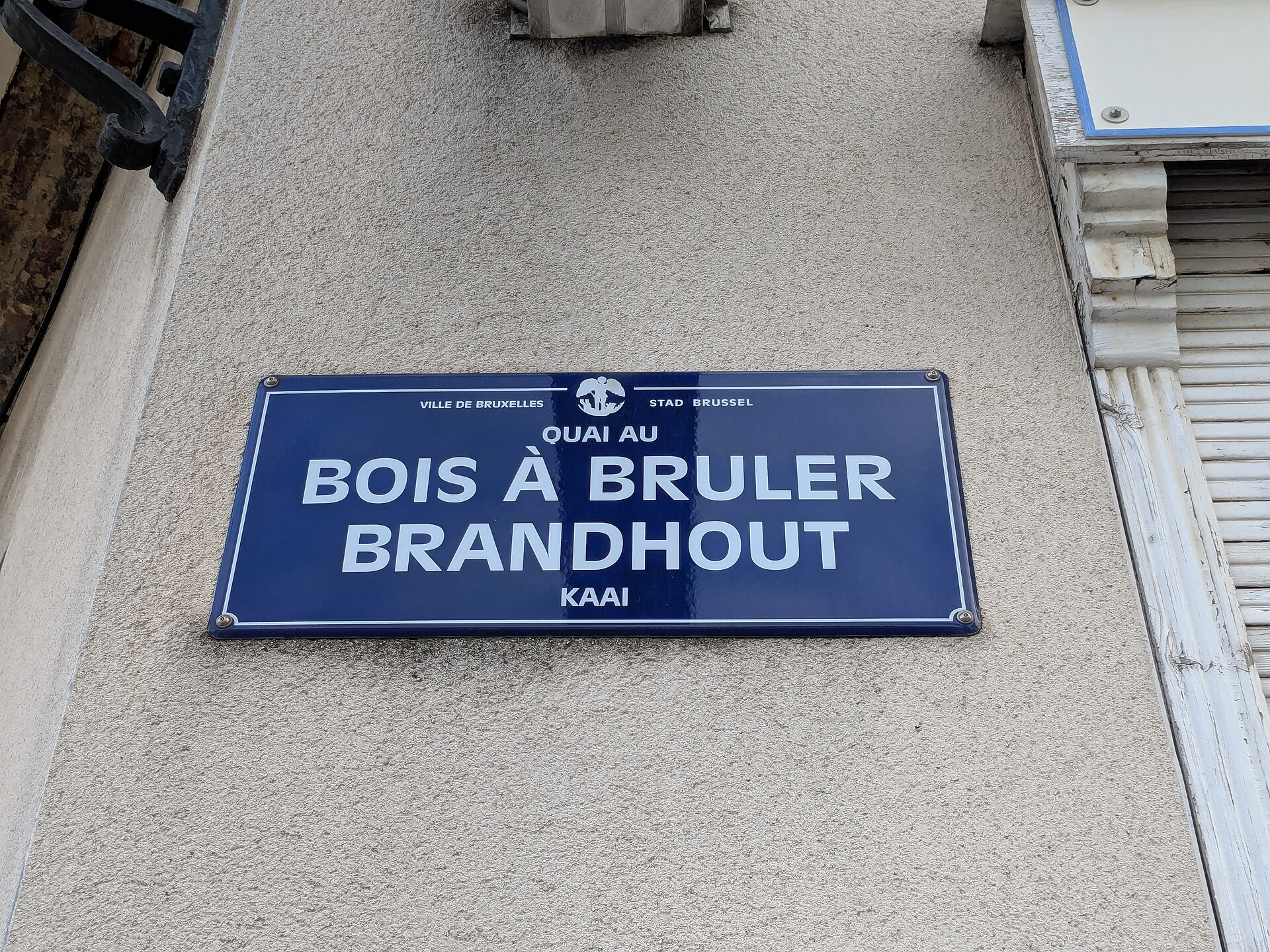 A blue Brussels street plaque pairs Quai au Bois a Bruler with Brandhoutkaai on a pale exterior wall.