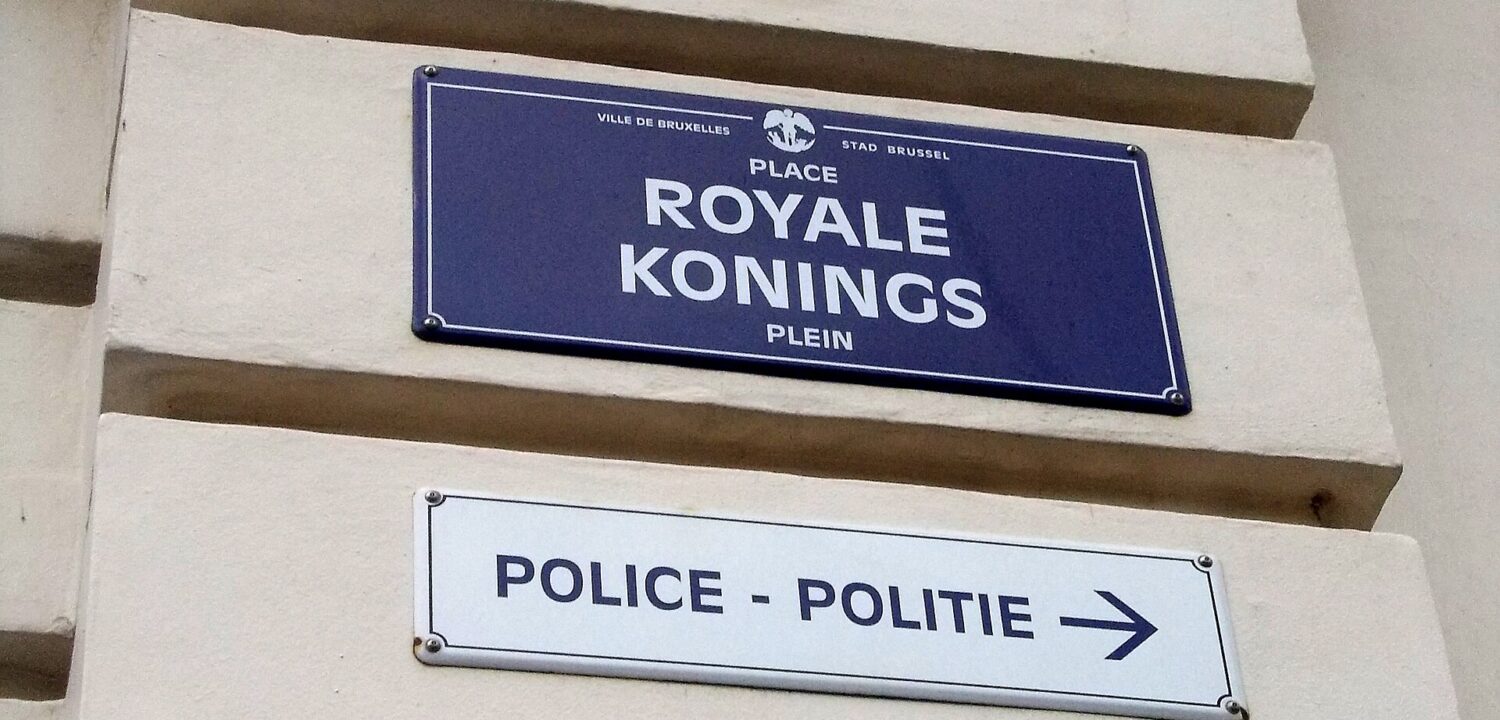 A blue Place Royale and Koningsplein street sign hangs above a bilingual police direction sign in Brussels.