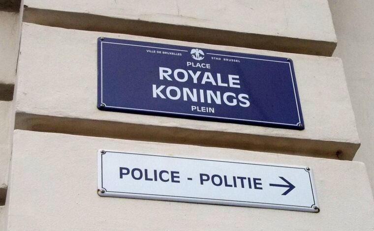 A blue Place Royale and Koningsplein street sign hangs above a bilingual police direction sign in Brussels.