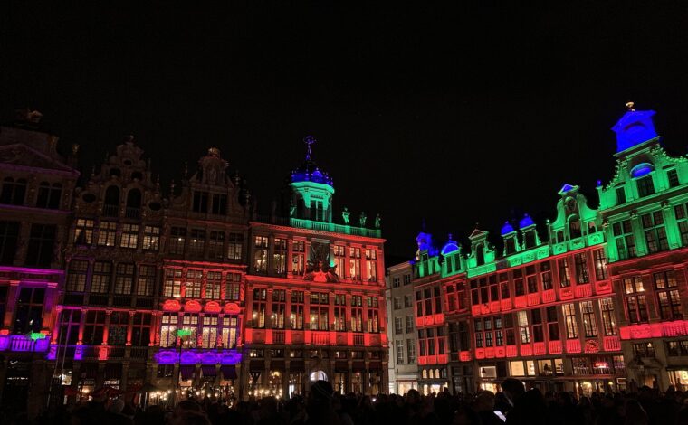 Brussels Grand-Place guild houses glow red, green and blue above a crowd watching the Winter Wonders lights at night.