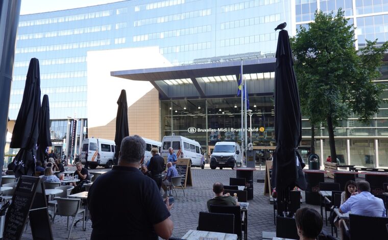 Brussels-Midi station signage appears above a glass entrance beyond outdoor cafe tables and parked police vans.