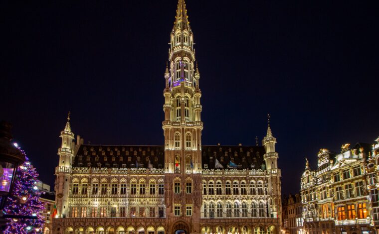 Brussels Town Hall glows above visitors on the Grand-Place at night, with gilded guildhouses beside its Gothic tower.