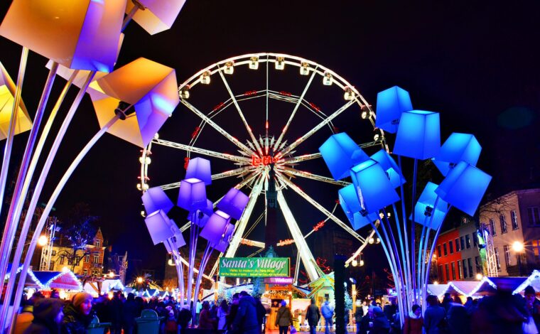 Brussels Winter Wonders Ferris wheel towers over festive chalets and visitors, framed by blue and gold illuminated sculptures at night.