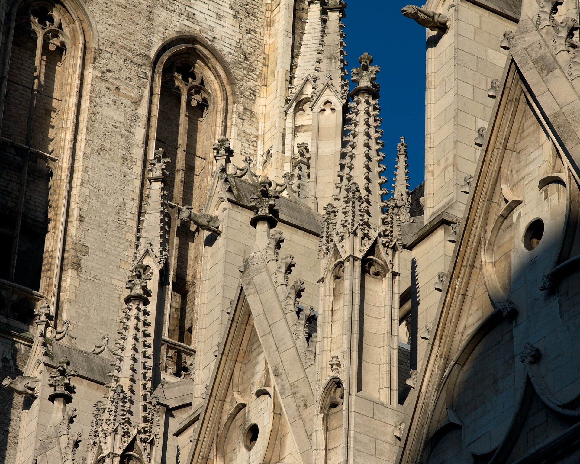 Carved pinnacles, gargoyles and pointed gables decorate the Cathedral of St Michael and St Gudula in Brussels beneath blue sky.