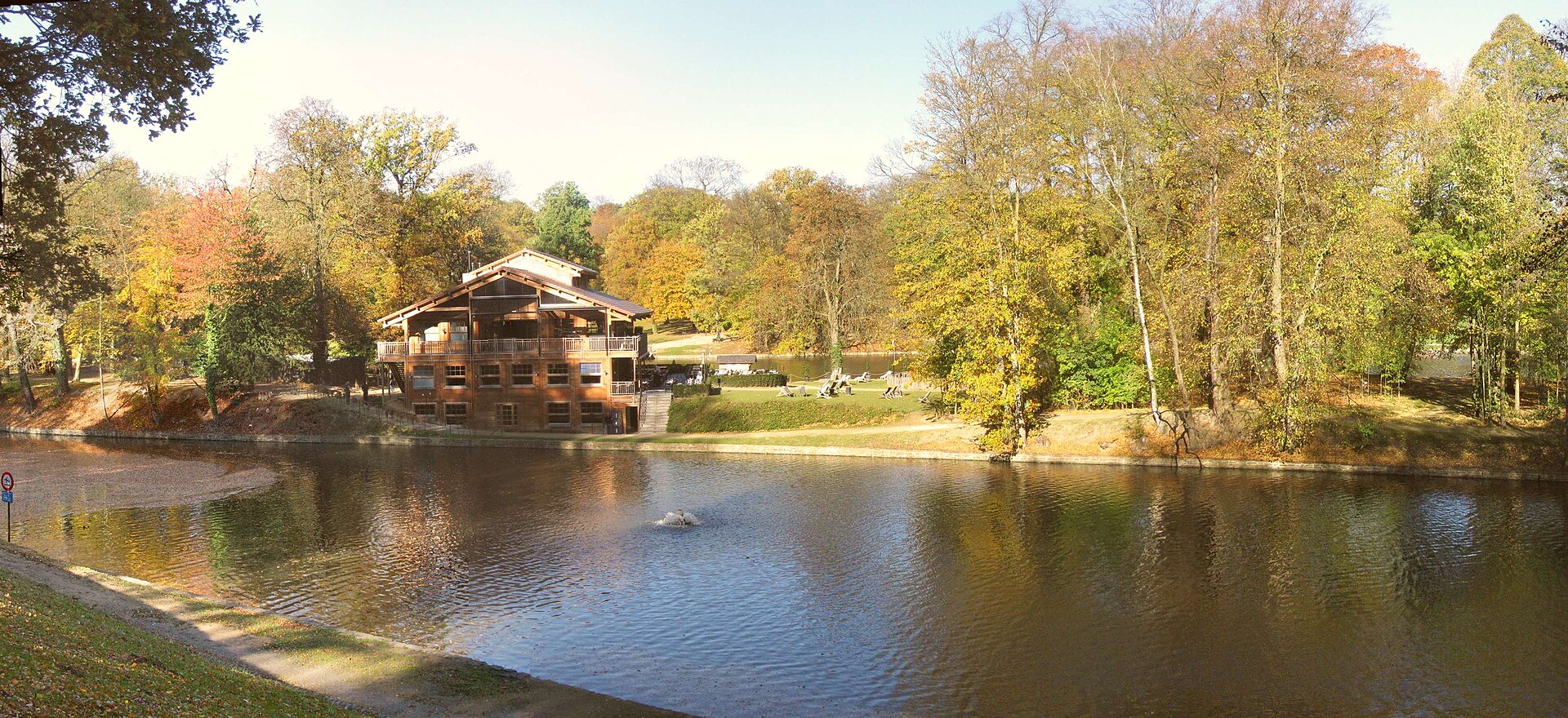 Chalet Robinson stands across the lake on Robinson Island in Brussels, surrounded by autumn trees and waterside seating.