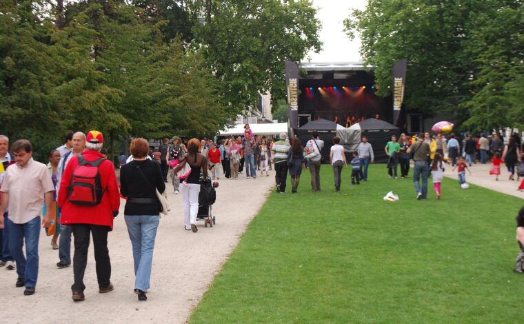 Children play on a lawn as families stroll past an outdoor stage in Brussels Park during National Day celebrations.