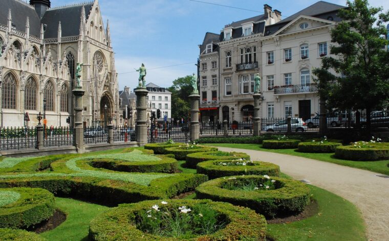 Clipped hedges and bronze statues frame Notre-Dame du Sablon across the street from the Petit Sablon garden in Brussels.