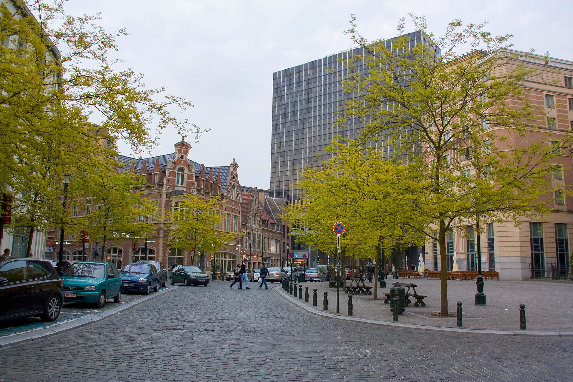 A cobbled street behind Sainte-Catherine church in Brussels passes gabled brick buildings, leafy trees and a visible metro entrance sign.