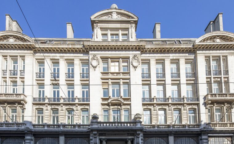 Cream-coloured Beaux-Arts facade of the Hotel Astoria on Rue Royale in Brussels, with balconies, carved pediments and the hotel name above the entrance, under a blue sky