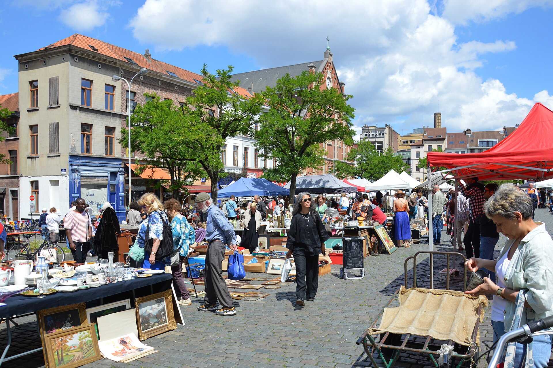 Crockery, framed pictures and shoppers fill Brussels Place du Jeu de Balle, with colourful canopies and the church behind leafy trees.