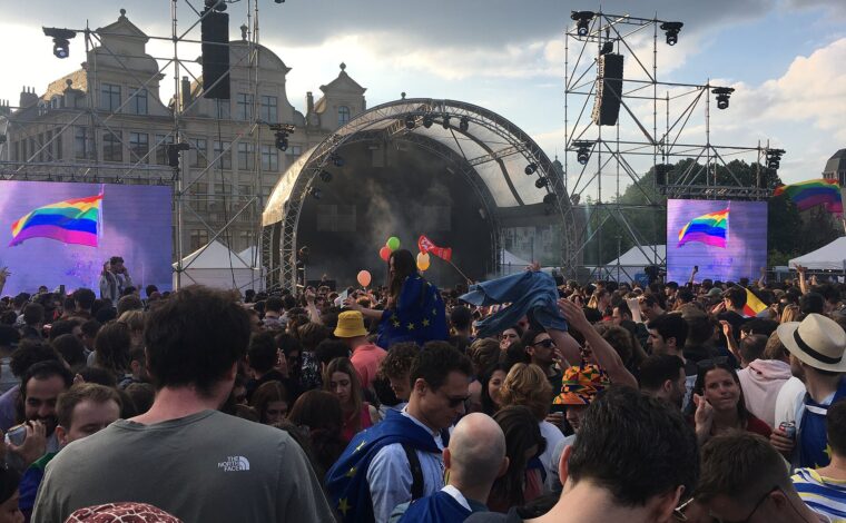 Crowds gather before a stage and rainbow flag screens during Brussels Pride 2023 in the city centre.