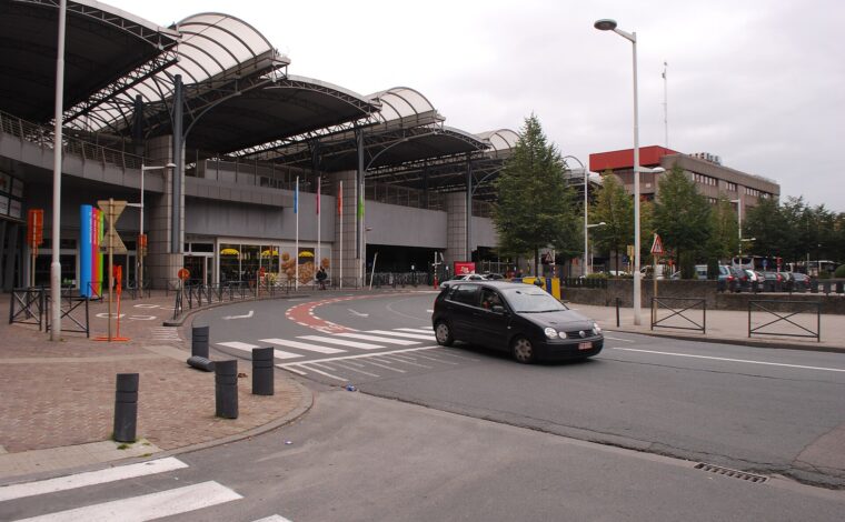 Curved canopies cover the Brussels-Midi station entrance beside a pedestrian crossing and a car on Rue de France.