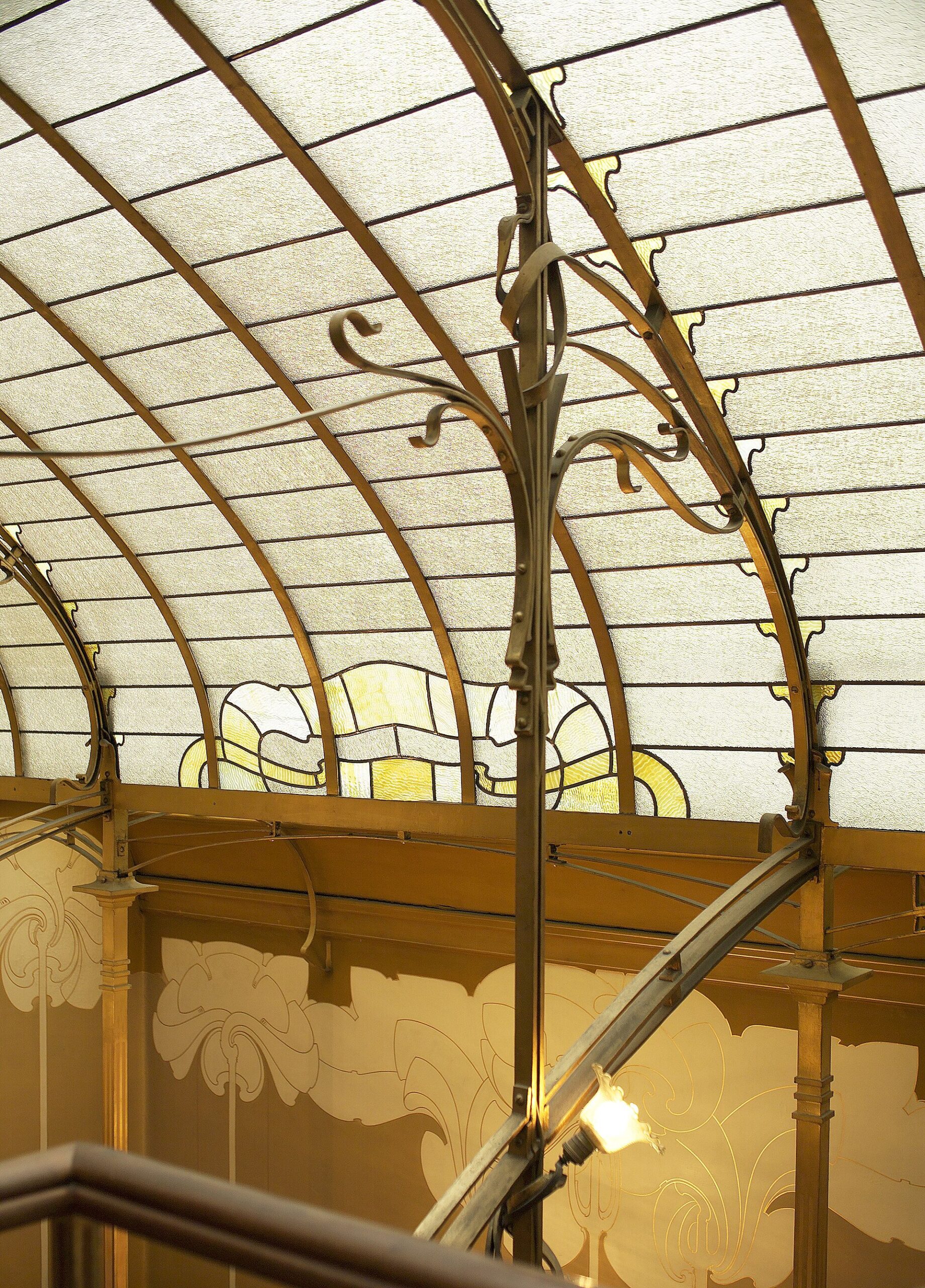 A curved glass skylight and branching metal supports illuminate the decorated stairwell of the Horta Museum in Brussels.