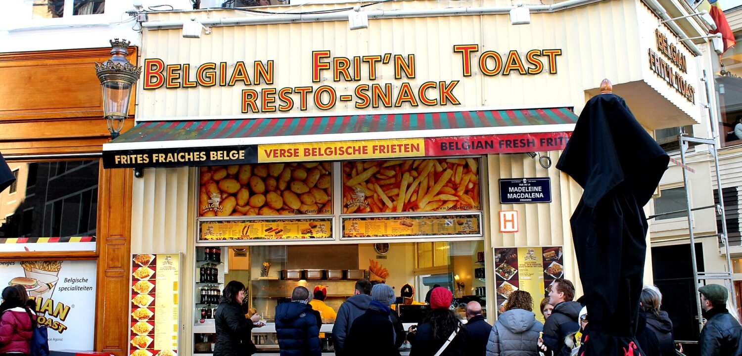 Customers queue for Belgian frites beneath a yellow shop sign on Rue de la Madeleine in central Brussels.