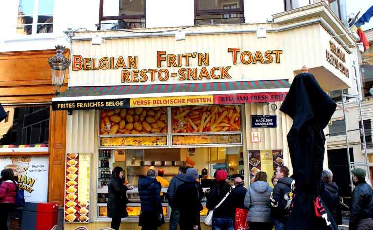 Customers queue for Belgian frites beneath a yellow shop sign on Rue de la Madeleine in central Brussels.