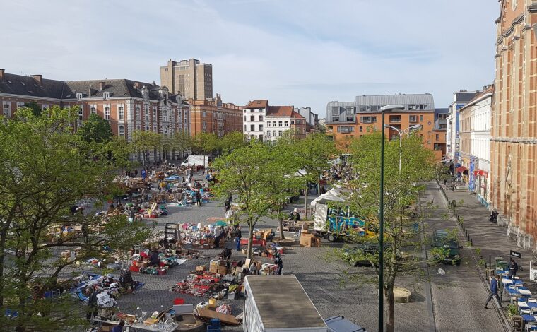 An elevated view shows secondhand stalls spread across Brussels Place du Jeu de Balle, between trees and historic buildings.