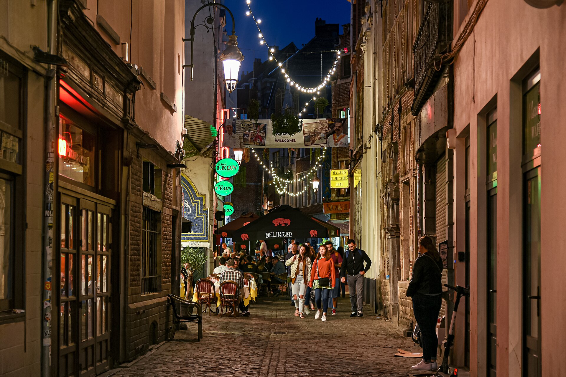 Evening diners and pedestrians fill Rue des Bouchers in Brussels beneath strings of lights, restaurant signs and narrow historic facades.