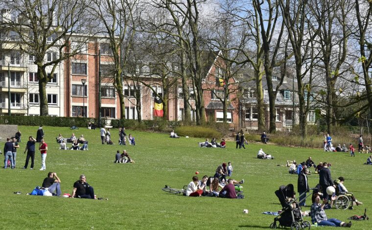 Families and friends relax on Josaphat Park’s sunny lawn in Brussels, with strollers, bicycles and budding trees around them.