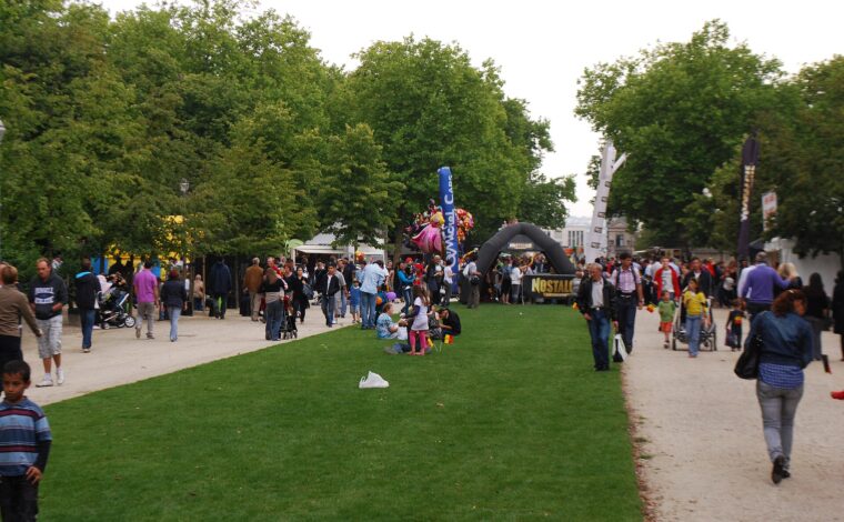 Families walk beside lawns and festival stalls in Brussels Park, with balloons and strollers among the National Day crowds.