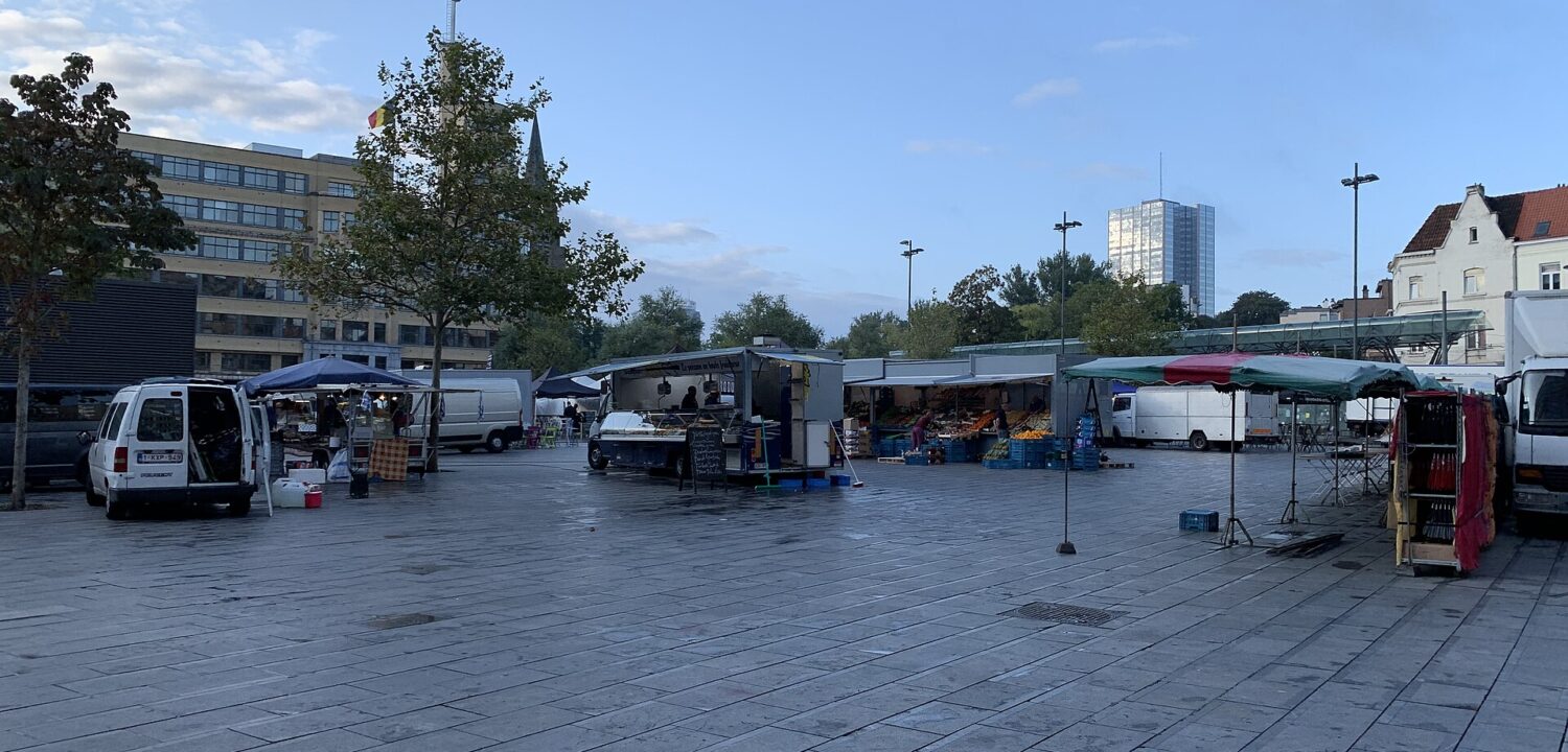 Food vans and produce stalls line Brussels Place Flagey in the morning, with the Flagey building beside the open paved square.