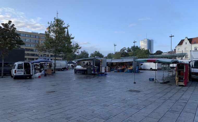 Food vans and produce stalls line Brussels Place Flagey in the morning, with the Flagey building beside the open paved square.