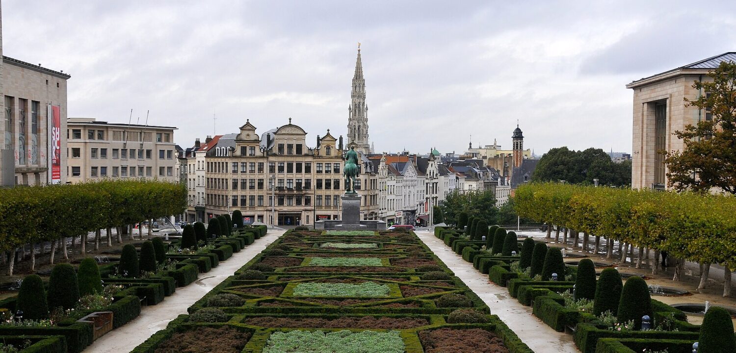 Formal gardens at Mont des Arts frame Brussels' town hall spire beyond an equestrian statue beneath an overcast sky.