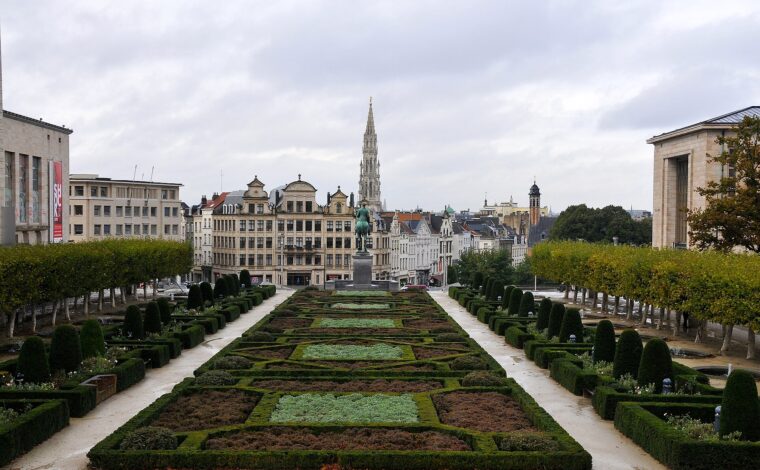 Formal gardens at Mont des Arts frame Brussels' town hall spire beyond an equestrian statue beneath an overcast sky.