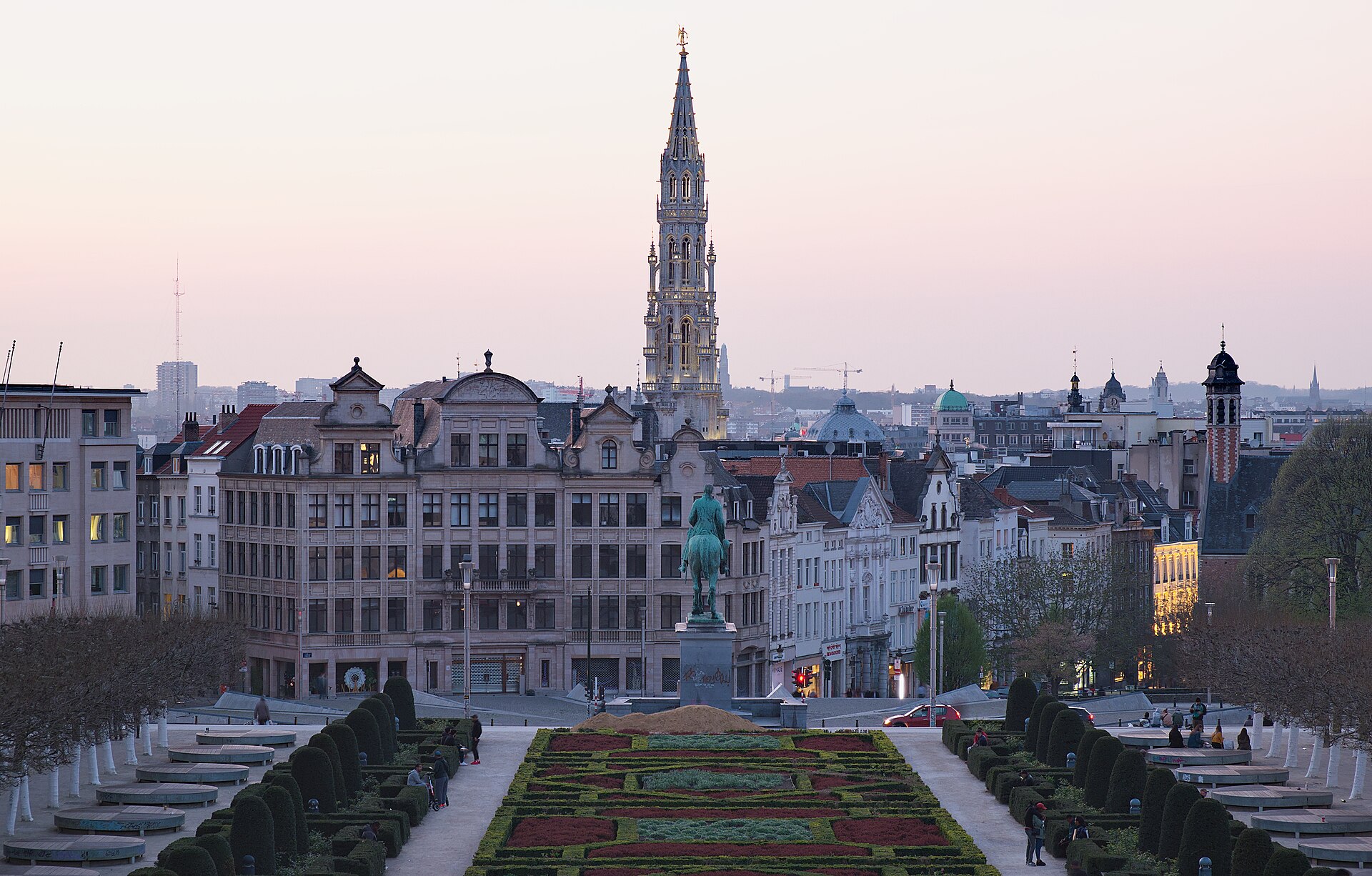 The formal Mont des Arts garden in Brussels leads toward the Town Hall spire under a pale pink twilight sky.